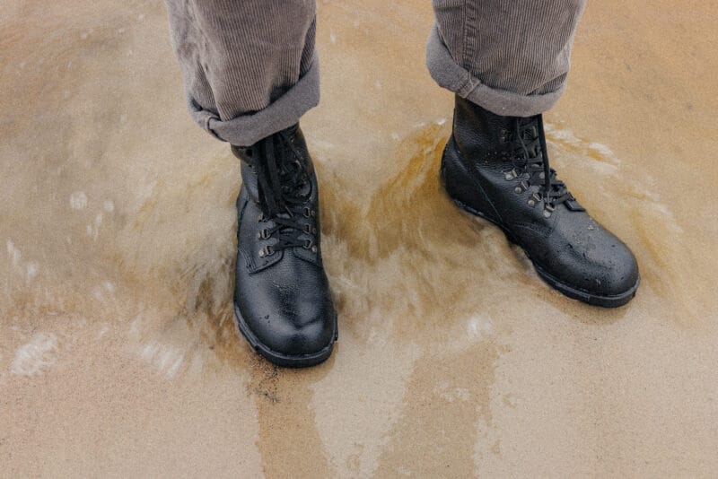 Black Samelin M77 Norwegian combat boots in full-grain leather worn on wet sand, demonstrating water-resistant durability and rugged grip