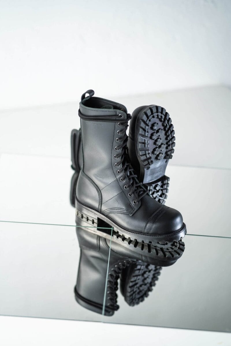 Black high aviator leather boots with rugged lug sole detail, angled view showing tread pattern and reflection for durable military-style outdoor wear